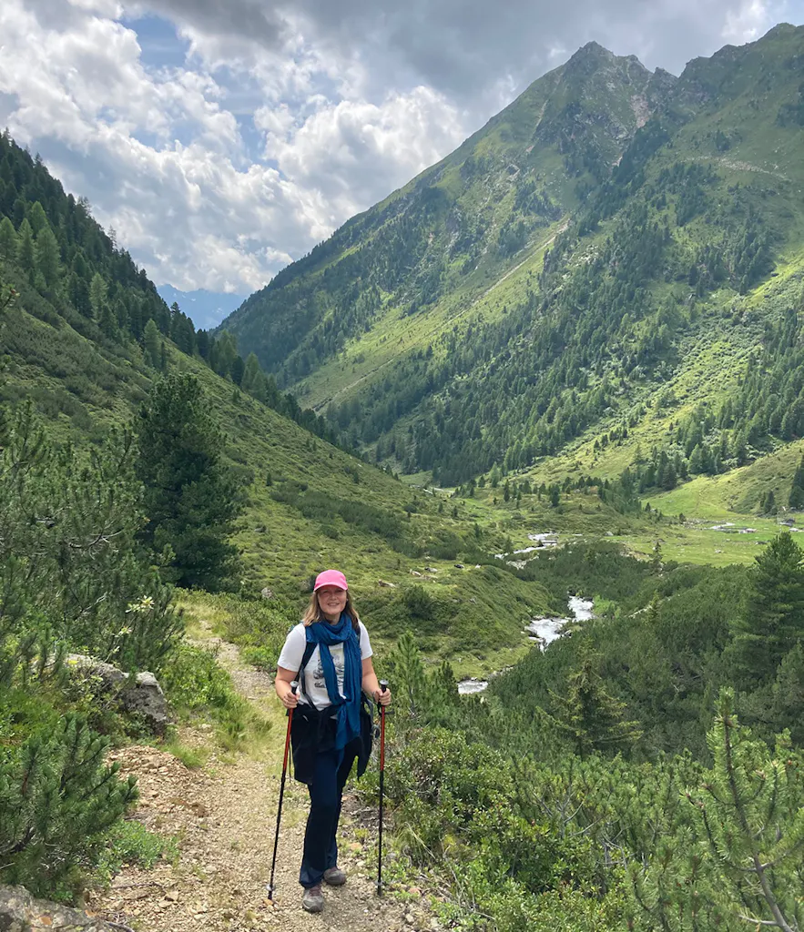 autorė su vaikščiojimo lazdomis kalnų fone